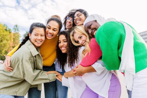 A diverse group of females smiling and hugging each other.