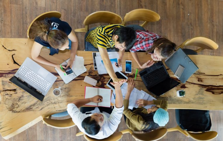 Group of young students in cooperation with their academic assignment. Top view shot of young people studying together around a table. students together at school table working homework and have fun.
